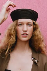 Gorro tipo casquete de diseño circular, confeccionado en tejido de punto trenzado en color marrón oscuro.