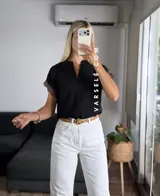 Blusa negra de tela Cey, con cuello mao y escote en V con cierre. Mangas cortas con detalle de encaje marrón en los hombros.