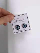 Aros tipo broquel con diseño de ojo turco circular en tonos azul, blanco y negro, montados sobre base de acero quirúrgico.