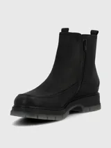 Bota corta tipo Chelsea de cuero negro, con elásticos laterales y suela track gruesa de goma translúcida gris.