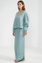 Pantalón celeste de lino italiano, de pierna ancha, con cintura elástica ajustable con cordón, bolsillos laterales y cortes redondeados en los laterales.