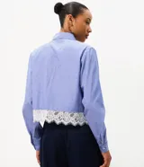 Camisa cropped azul con rayas diplomáticas blancas, cuello clásico, mangas largas y detalle de encaje blanco aplicado en el borde inferior.