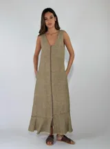 Vestido largo sin mangas de lino color beige, con escote en V, cierre frontal completo y bolsillos laterales. Cuenta con detalle de volados en el bajo con terminaciones deshilachadas.