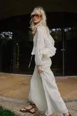 Blusa de escote en pico y manga larga con puños elásticos. Presenta un diseño semitransparente con bordados florales a tono, cintura elástica y cierre frontal mediante lazos con abalorios decorativos.
