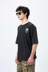 Remera negra de corte holgado con mangas cortas amplias y cuello redondo. Estampado pequeño de flor en el pecho y estampado grande en la espalda con diseño floral y texto.