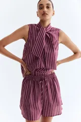 Short holgado de tela liviana color morado con finas rayas verticales blancas. Presenta cintura elástica fruncida con cordón ajustable y bajo redondeado con aberturas laterales.