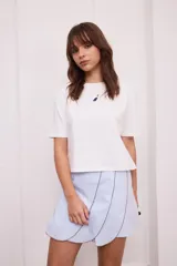 Falda corta de corte cruzado en color celeste, con diseño de paneles superpuestos con bordes en contraste. Cuenta con cierre lateral.