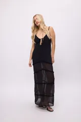 Vestido largo de estilo maxi, confeccionado en chiffon negro con transparencias. Presenta un diseño con volados en los recortes horizontales, escote con tiras ajustables y breteles finos.