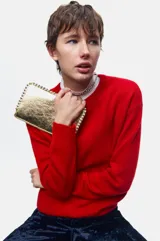 Cartera pequeña color dorado metálico con cierre superior. Presenta tachas plateadas decorativas a lo largo de los bordes superior e inferior.