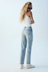 Jeans wide leg de tiro alto y cinco bolsillos, confeccionados en denim con lavado azul medio y efecto desgastado. Presenta cierre frontal con cremallera y botón metálico.