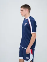 Remera deportiva de entrenamiento Umbro del Club Nacional de Football, color azul marino con detalles en blanco y líneas rojas en los hombros. Cuenta con el logo de la marca y el escudo del club en el pecho.