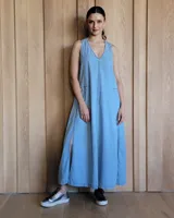 Vestido largo de jean color celeste, con escote en V, sin mangas y aberturas laterales en la falda. Incluye bolsillos laterales.