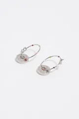 Caravanas de metal plateado con aros argolla adornados con pequeños detalles esmaltados de colores y un dije colgante circular con un corazón recortado en el centro y letras esmaltadas alrededor.