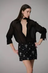 Camisa de organza negra con diseño semitransparente, cuello camisero clásico, mangas largas con puños estructurados y cierre frontal con botones.