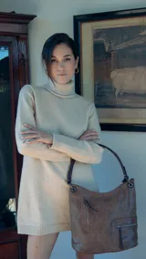 Cartera estilo hobo de color marrón con textura símil cuero, cuenta con dos bolsillos frontales con cierre metálico, apertura superior con cierre, correa corta para el hombro y correa larga desmontable y regulable.