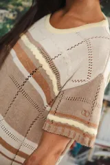 Vestido largo de tejido calado con rayas horizontales en tonos beige, marrón y amarillo. Tiene corte recto, hombros caídos, tajo lateral y logo bordado en la manga.