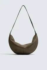 Bolso de hombro con diseño de media luna, confeccionado en gamuza color marrón. Cuenta con un compartimento principal con cierre de cremallera y un bolsillo interior con cierre. Posee un asa de hombro integrada.