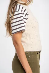 Chaleco de punto sin mangas en color beige melange con motas oscuras. Presenta cuello redondo y terminaciones acanaladas en el ruedo y las sisas.