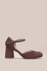 Zapato de tacón color bordó, confeccionado en terciopelo suave, con diseño de pulsera en el tobillo y cierre de hebilla. La punta es cerrada y presenta detalles de líneas cosidas. El tacón es ancho y forrado, con una altura de 7 cm.