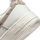 Championes Nike Air Force 1 de corte bajo, color blanco con detalles en textura de piel de serpiente en tono bronce en el swoosh lateral y en el talón.
