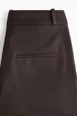 Pantalón sastrero de sarga marrón, de corte recto y tiro medio, con cintura clásica, trabillas para cinturón, bolsillos al bies y pliegues frontales.