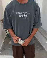 Remera marrón oversize con cuello redondo y mangas cortas. Estampado frontal con el texto "Uruguay Run Club" en celeste y siluetas blancas de personas corriendo.