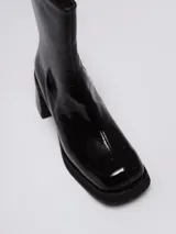 Botas de caña media con acabado charolado brillante, punta cuadrada y taco bloque. Cuentan con cierre lateral interno para facilitar su colocación.