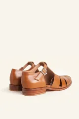 Sandalias de cuero color marrón, tipo romanas, con talón cerrado, tira en T con detalles de tachas metálicas, aberturas laterales y cierre de hebilla ajustable. Tienen tacón bajo de madera.