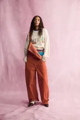 Mameluco de denim color naranja con tirantes ajustables, bolsillos de plastrón en el pecho y bolsillos laterales. Cuenta con cierre de ganchos metálicos en el delantero y botones en los laterales.