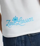 Remera de algodón con cuello redondo y mangas cortas. Presenta un estampado frontal con lettering 'Lush Life' y un delfín en estilo aerógrafo con colores vibrantes.