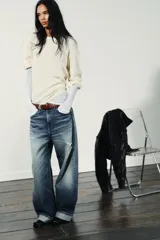 Jeans de mezclilla azul con lavado desgastado y rotos en la pierna derecha. Tienen tiro medio, corte ancho (baggy) y puños doblados en el bajo.