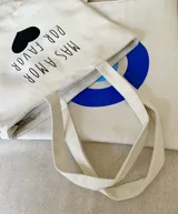 Tote bag de tela color blanco con estampado frontal de texto y corazón negro. Cuenta con cierre principal y bolsillo interno.