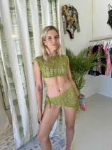 Pareo corto de tejido crochet en color verde, con diseño de red y ajuste lateral mediante nudo.