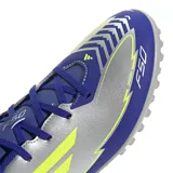 Championes de fútbol Adidas F50 Club TF, modelo inspirado en Lionel Messi, diseñados para superficies sintéticas. Presentan una combinación de colores azul, gris y detalles en amarillo neón, con suela de multitacos para mayor tracción.