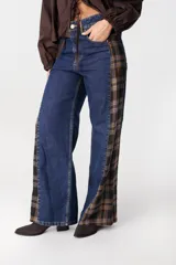 Jean de pierna ancha con diseño bicolor, combinando denim azul clásico con un panel lateral de tela a cuadros en tonos marrón y negro. Presenta cuatro bolsillos funcionales y cierre frontal.