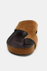 Sandalia plana tipo chinela confeccionada en serraje color marrón, con diseño de pala ancha y separador para el dedo. Cuenta con suela de plataforma baja y punta redonda.