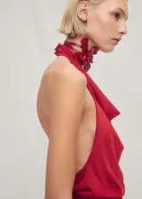 Top de punto fino color rojo con diseño de cuello halter drapeado y espalda descubierta. Presenta un cierre de botones en el cuello y un bajo asimétrico.