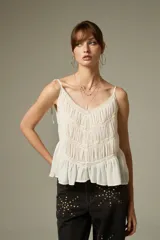 Musculosa negra de breteles finos, confeccionada en algodón con diseño plisado y detalles de encaje. Presenta un corte holgado con volados en el ruedo y escote profundo.