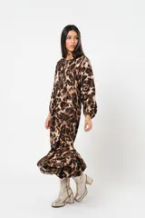 Vestido midi de corte holgado con estampado animal print en tonos marrones y beige. Tiene cuello redondo con lazo, mangas largas abullonadas y falda amplia con volantes. Incluye cinturón marrón con tachas.
