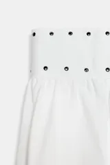 Falda midi blanca de tiro medio con detalle de tachas metálicas en la cintura y bajo tipo globo. Cierre lateral con cremallera oculta.