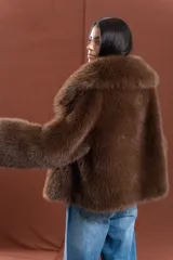 Tapado de piel sintética en color marrón chocolate, con diseño de corte amplio y largo a la cadera. Presenta un cuello envolvente de gran volumen y mangas largas, con interior forrado.