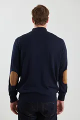 Sweater de punto gris con medio cierre frontal, cuello alto y coderas en tono marrón. Presenta un diseño clásico con puños y ruedo acanalados.