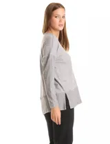 Buzo de calce suelto confeccionado en tejido melange de punto suave, con escote en V, mangas largas con hombros caídos y detalles de tejido rib en puños y ruedo. Presenta aberturas laterales y un diseño asimétrico con la parte posterior ligeramente más larga.