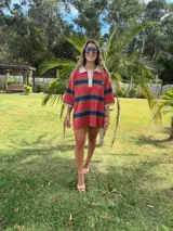 Remerón de algodón a rayas horizontales en tonos rojo, marrón y azul. Tiene cuello tipo polo con botones y mangas cortas.