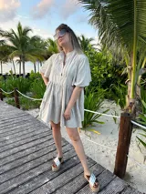 Vestido corto color beige de lino, con cuello mao, mangas cortas con volados, tablas en el canesú y falda escalonada con volantes.