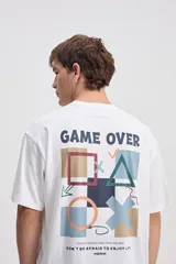 Remera oversize blanca de algodón con estampa en la espalda inspirada en controles de videojuegos y frases decorativas.