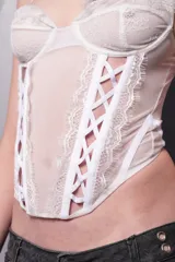 Corset blanco de microtul y encaje con tazas de encaje forradas con microtul y puntilla en el borde al tono con aro metálico interno media copa. Terminación inferior y en tazas con puntilla al tono. Detalle de cortes en el cuerpo con ballenas acompañando la unión. Detalle de elástico bretel en zigzag entre las ballenas delanteras. Terminaciones con elástico partido y breteles elásticos regulables. Acceso por espalda mediante ganchos corseteros.