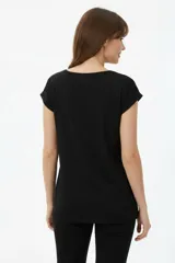 Remera de algodón negra, de corte holgado, con cuello redondo a la base y detalle de estampado floral en el hombro izquierdo.