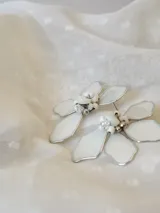 Par de aros colgantes con forma de flor blanca con borde plateado y centro de perlas y cuentas plateadas.