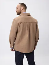 Sobrecamisa de paño color beige, con cuello clásico, cierre frontal con botones metálicos y bolsillos frontales. Presenta un diseño de corte recto y aberturas laterales en el ruedo.